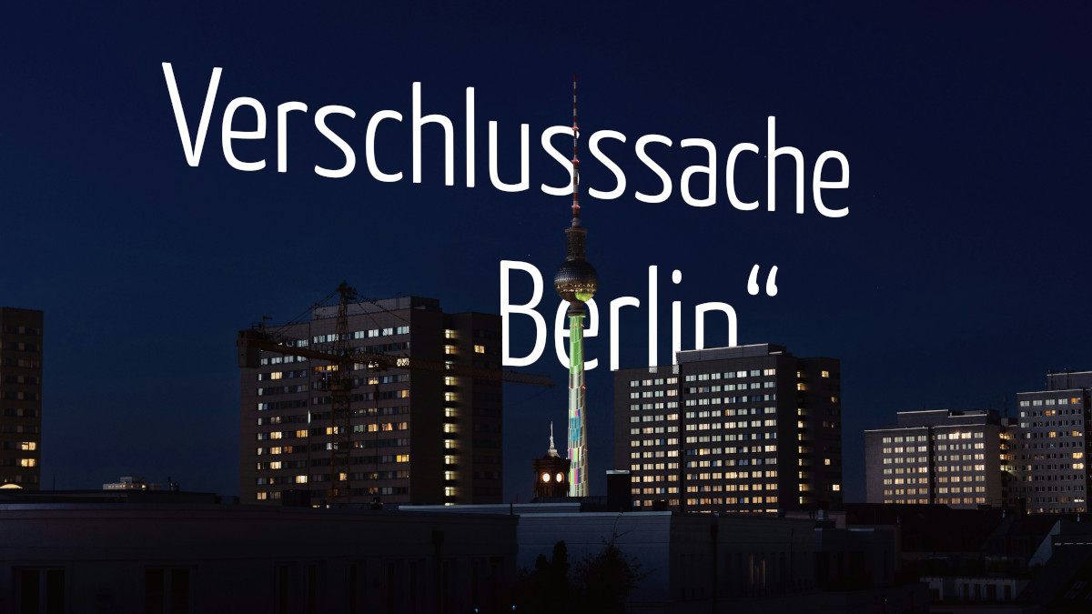 Weißer Schriftzug 'Verschlusssache „Berlin“' in einer abendliche Silhouette Berlins eingebettet. Vor dem Schriftzug ragen mehrere beleuchtete Hochhauskomplexe, das Rote Rathaus und der illuminierte Fernsehturm in den dunklen Nachthimmel.